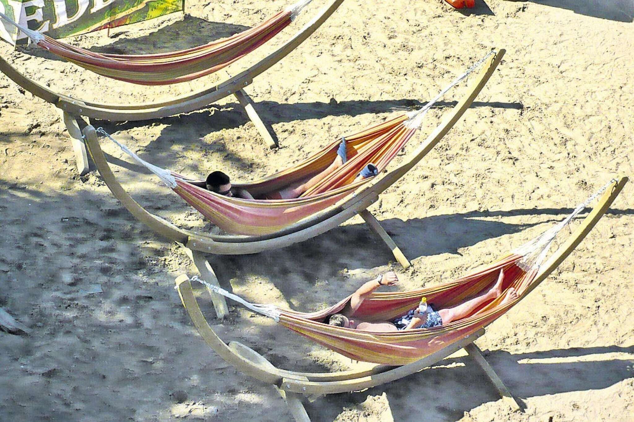 Three hammocks tied to a wooden frame on a sandy beach.