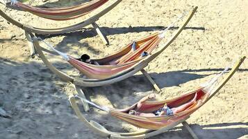 Three hammocks tied to a wooden frame on a sandy beach.