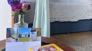 Ein Schlafzimmer mit einem Bett, einem Vorhang, einer Vase mit Blumen, einem Willkommensschild und einer Schachtel mit kleinen Kuchen.