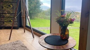 Ein Zimmer mit einem Teleskop, einer Zierdekorationsschrank, einer Blumenvase und Blick auf eine grüne Landschaft durch große Fenster.