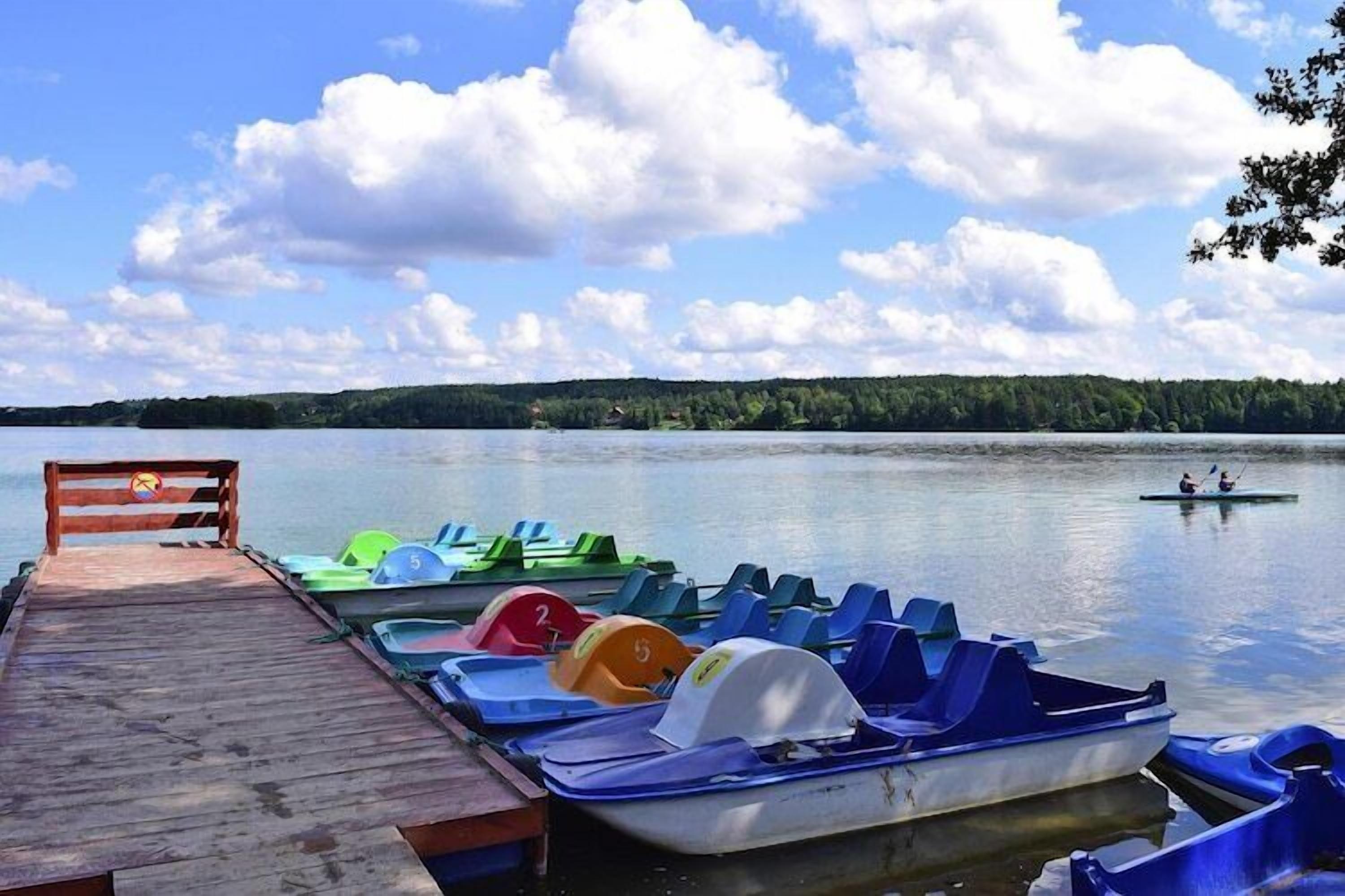 A wooden dock with colorful pedal boats and a rowboat on calm water.