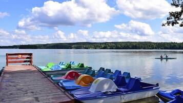 A wooden dock with colorful pedal boats and a rowboat on calm water.