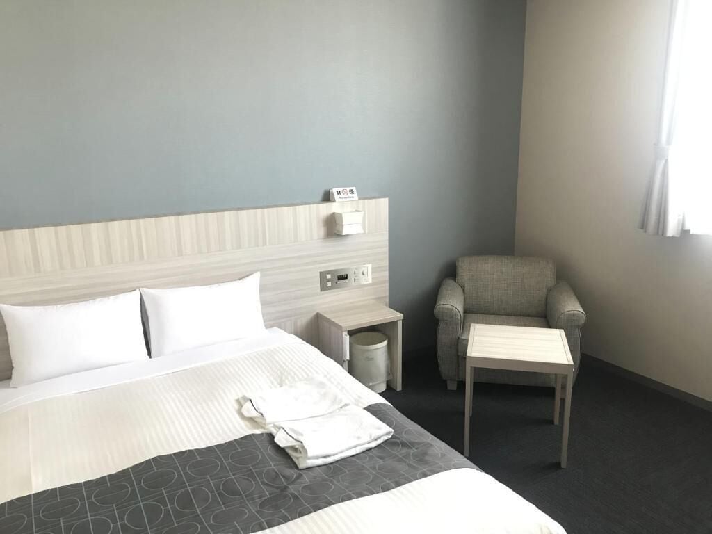 A hotel room with a bed, a chair, a small table, and a nightstand.