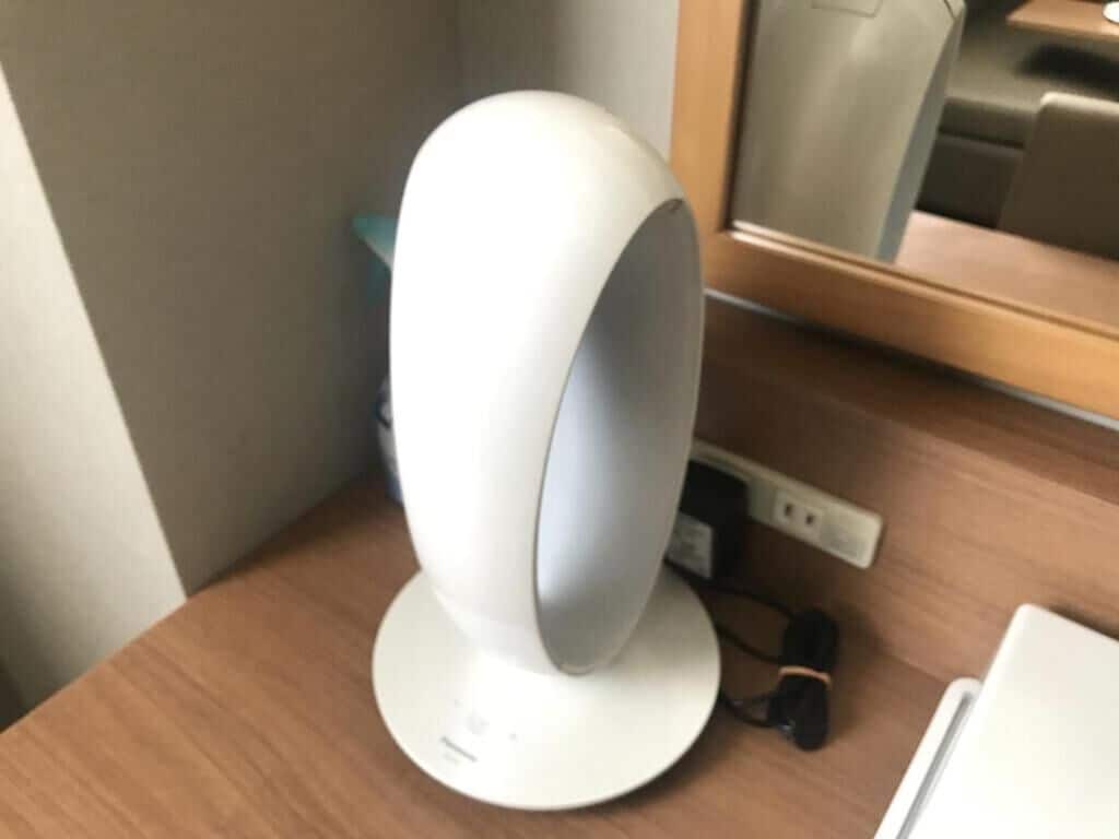 A white, modern, cylindrical device on a wooden surface, likely a speaker or similar electronic equipment.