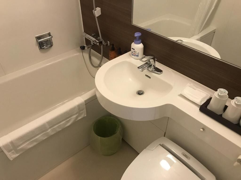 Un baño con lavamanos blanco, un espejo, un bote de basura verde y un inodoro.