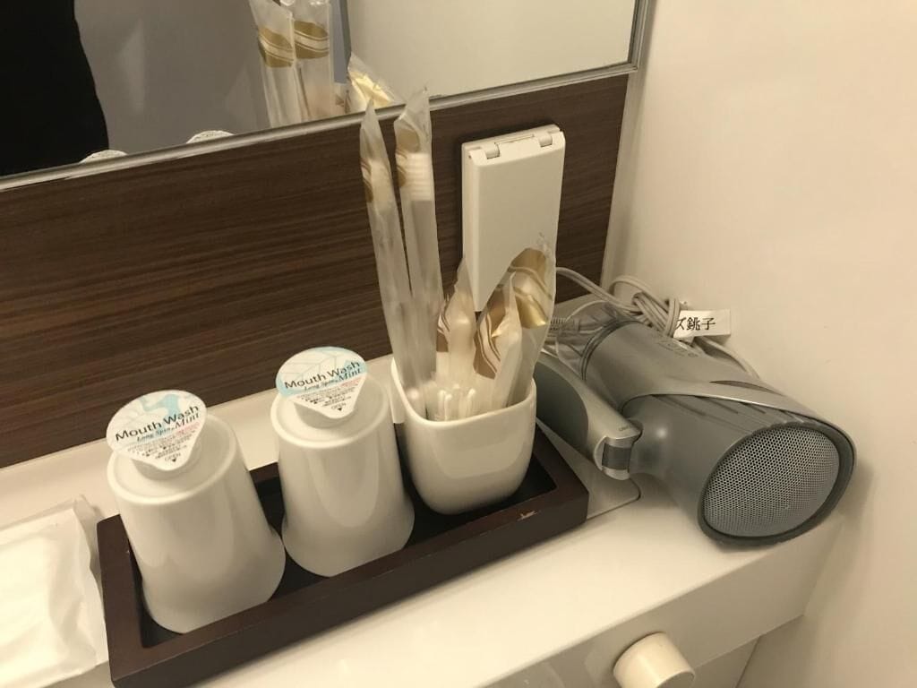 A bathroom vanity with a mirror, a hairdryer, and a tray with mouthwash bottles and a toothbrush holder.