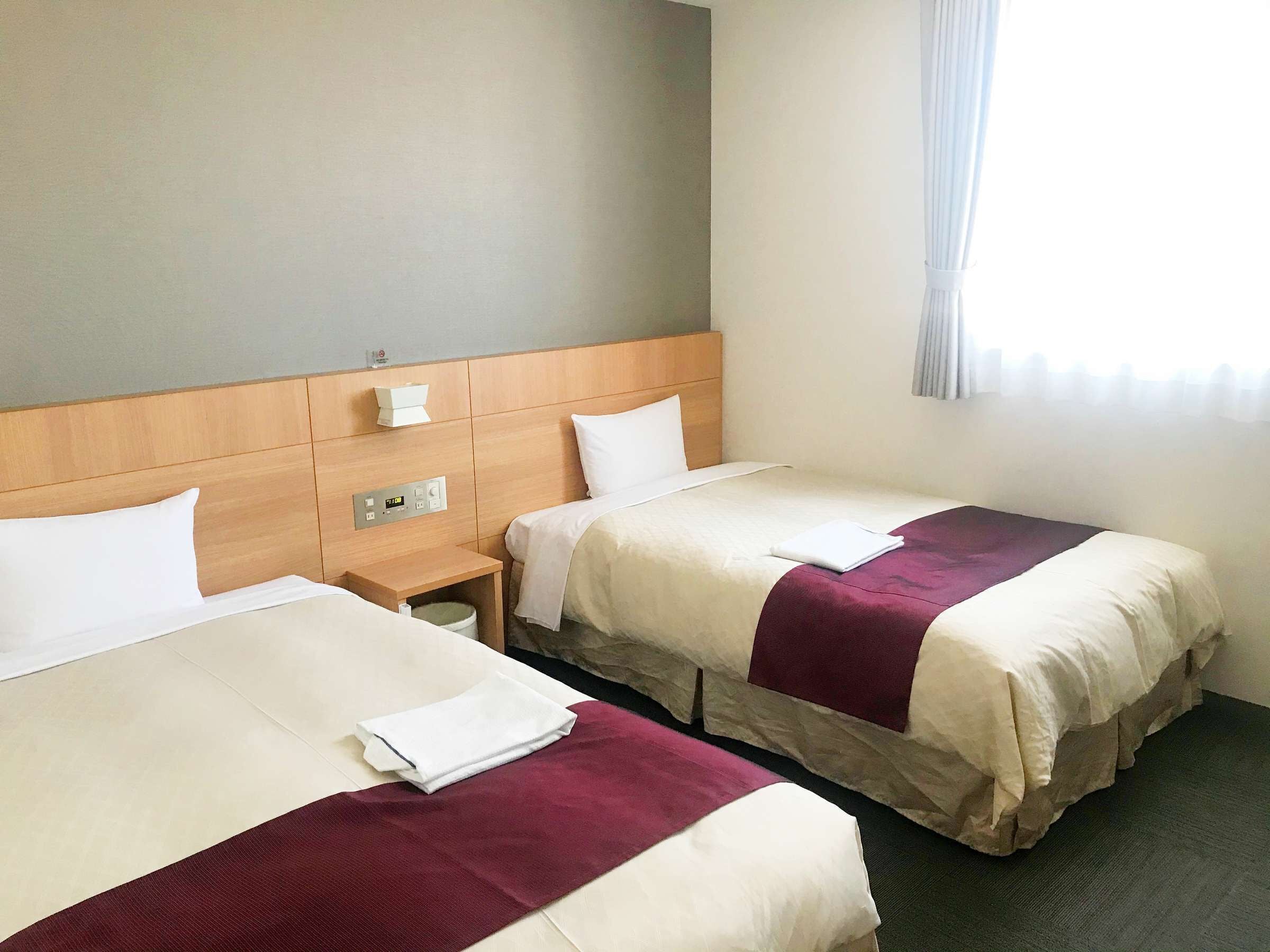 Habitación de hotel con dos camas, cabecero de madera, mesita de noche y ventana con cortinas.