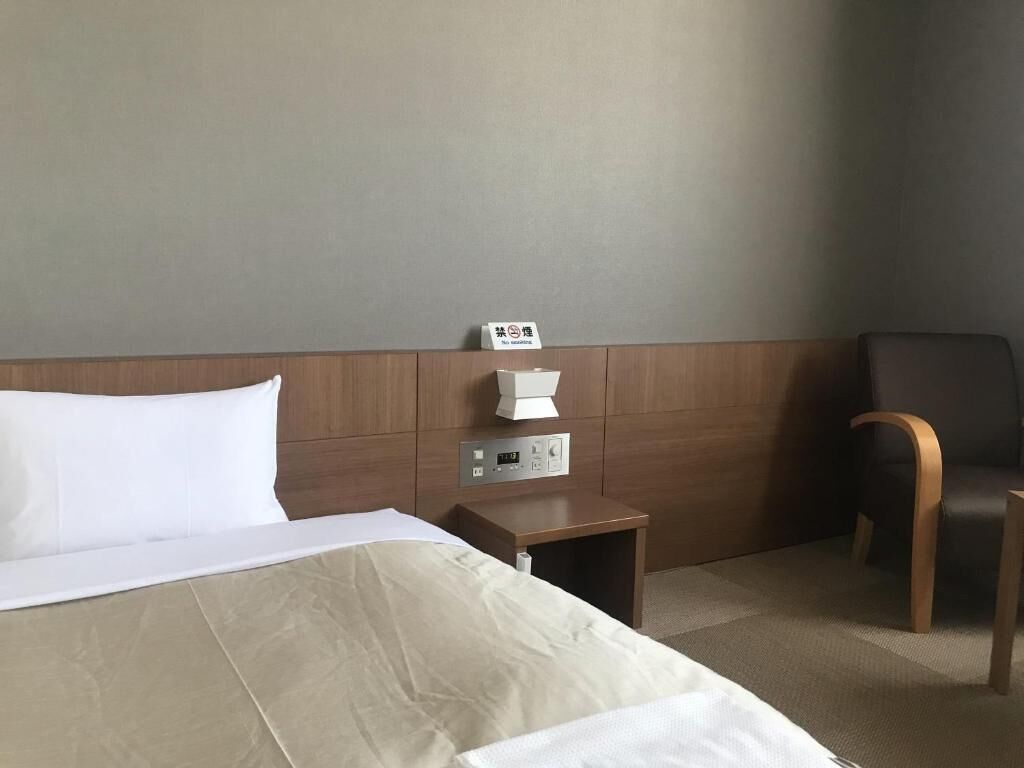 Une chambre d’hôtel comprenant un lit, une table de chevet avec un thermostat, une chaise et un panneau indiquant qu’il est interdit de fumer.