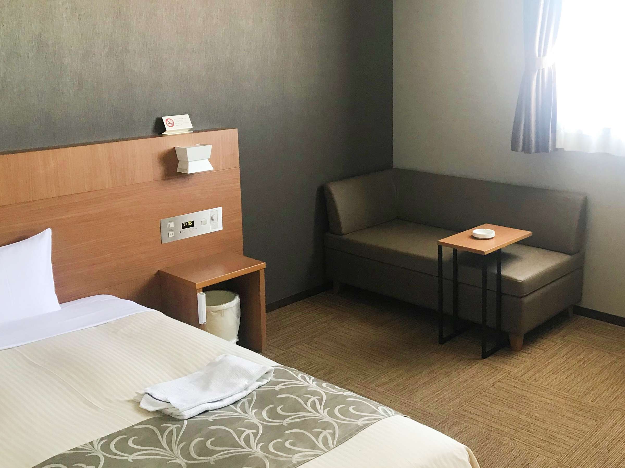 A hotel room with a bed, a bedside table, a small table with a plate, and a couch.