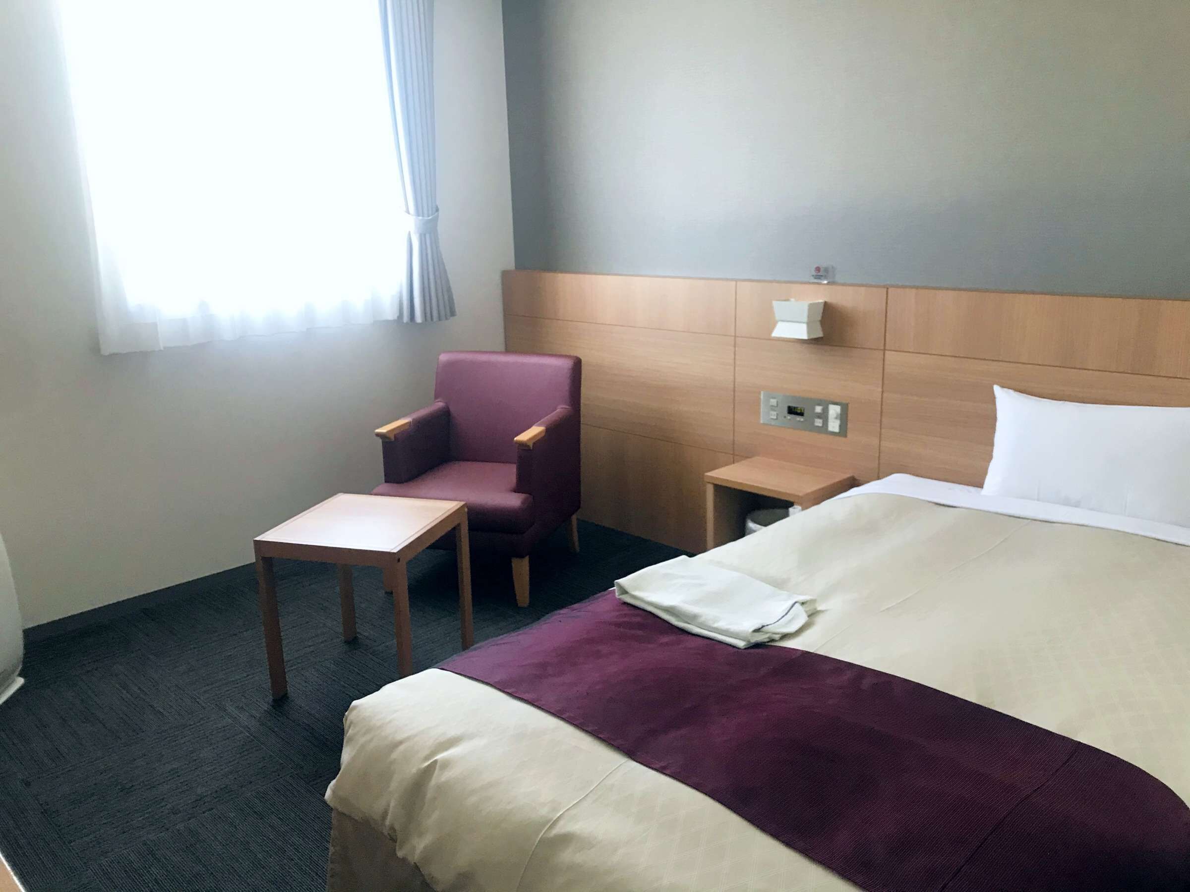 A hotel room with a bed, a chair, a small table, and a nightstand.