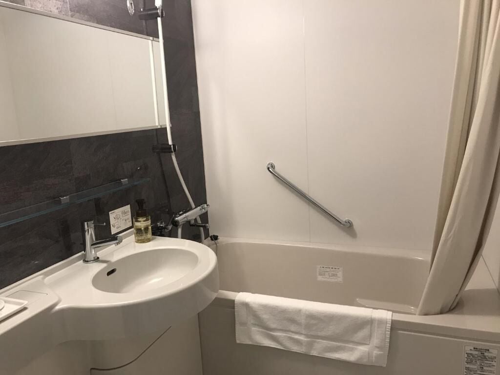 A bathroom with a sink, mirror, towel rack, and a grab bar near the shower.