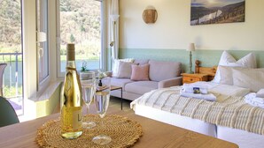 A hotel room with a bed, a sofa, a table with a bottle and glasses, and a view of the outdoors. - Apartment with balcony directly on the banks and with a view of the Moselle (Bullay)