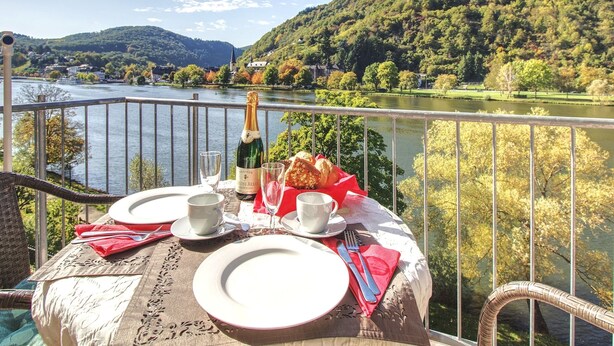A table set for two with a bottle of wine, glasses, and bread on a balcony overlooking a river and forested hills. - Apartment with balcony directly on the banks and with a view of the Moselle (Bullay)