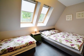 A small, well-lit room with two beds, a nightstand, and a window with a view of greenery. - Comfortable holiday apartment close to the beach (Rewal)