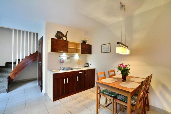 A compact kitchen with wooden cabinets, a dining table with chairs, and a staircase leading to another level.