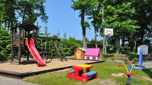 Une aire de jeux avec un toboggan, des balançoires et une petite maison.