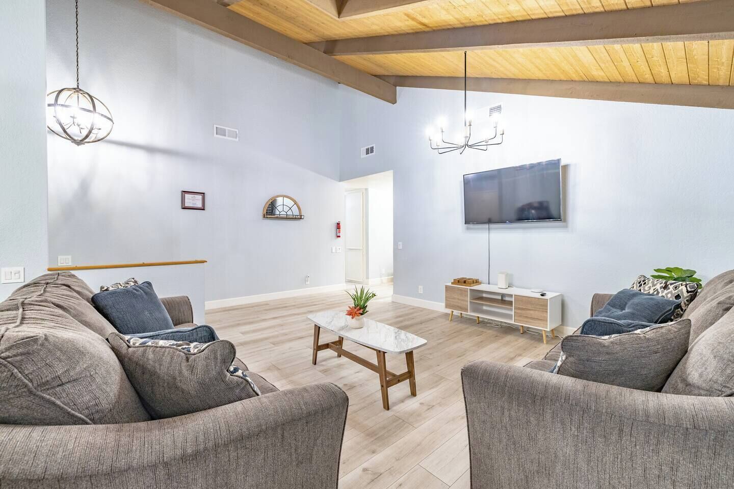 Een moderne woonkamer met grijze banken, een houten salontafel, een flatscreen televisie en een houten plafond.