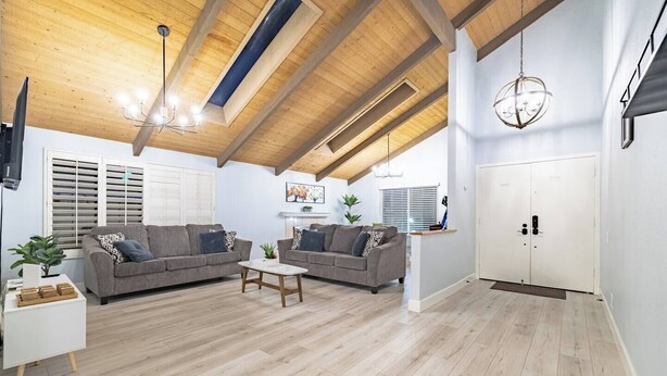 A spacious living area with two grey sofas, a coffee table, wooden flooring, a ceiling with exposed beams, and a white door.