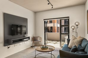 Uma sala de estar moderna com uma TV de tela plana na parede, um sofá azul, uma mesa de centro redonda e uma estante de livros.