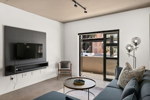 Uma sala de estar moderna com uma televisão de tela plana na parede, um sofá confortável, uma mesa de centro redonda e uma poltrona.
