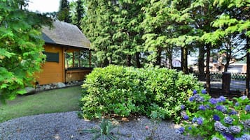 Une cabane en bois dotée d’un porche couvert, entourée d’une végétation luxuriante et bordée d’un chemin de gravier.