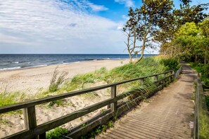 Une promenade en bois mène à une plage de sable, avec l’océan en toile de fond.