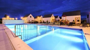 Une piscine entourée d’une terrasse, de chaises longues et d’une rangée de maisons avec des garages attenants.