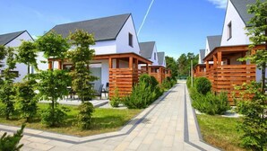 Une rangée de maisons modernes, blanches, avec des toits gris, des terrasses en bois et une végétation bien entretenue.