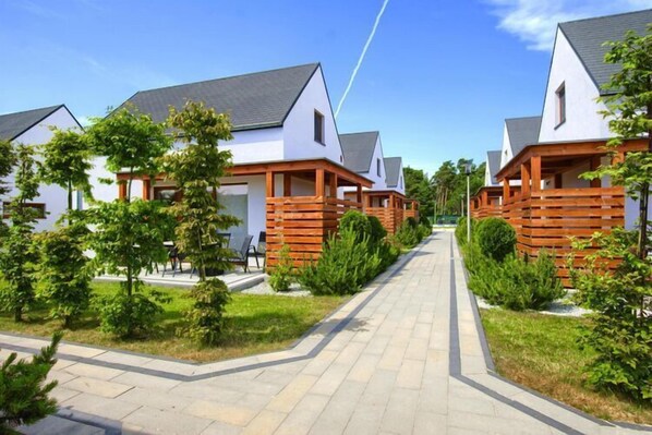 A row of modern, white houses with grey roofs, wooden decks, and well-maintained greenery.