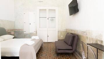 Una camera d'albergo con un letto, una sedia, un armadio e una TV fissata al muro.