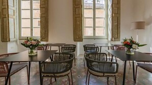 Ein Essbereich mit Tischen und Korbstühlen, große Fenster mit Rollläden und ein Blumenstrauß auf dem Tisch.