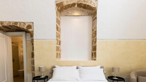 Ein Hotelzimmer mit einem Bett, zwei Nachttischen, einem Sessel und einer einzigartigen Steinbogenarchitektur darüber.
