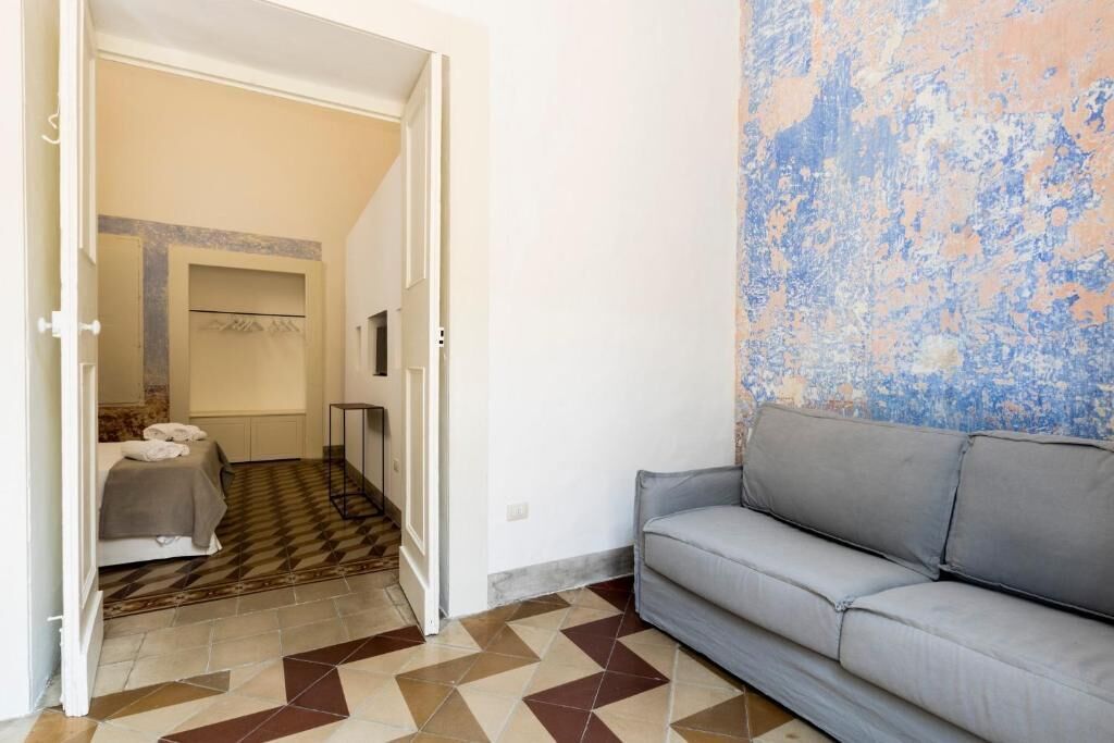 A room with a checkered floor, a grey sofa, and a wall with a textured pattern.