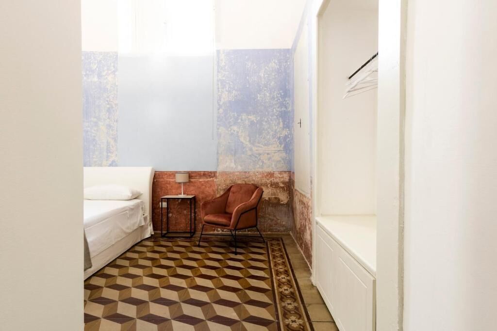 A small, compact room with a checkered floor, a single bed, a chair, and a small table.