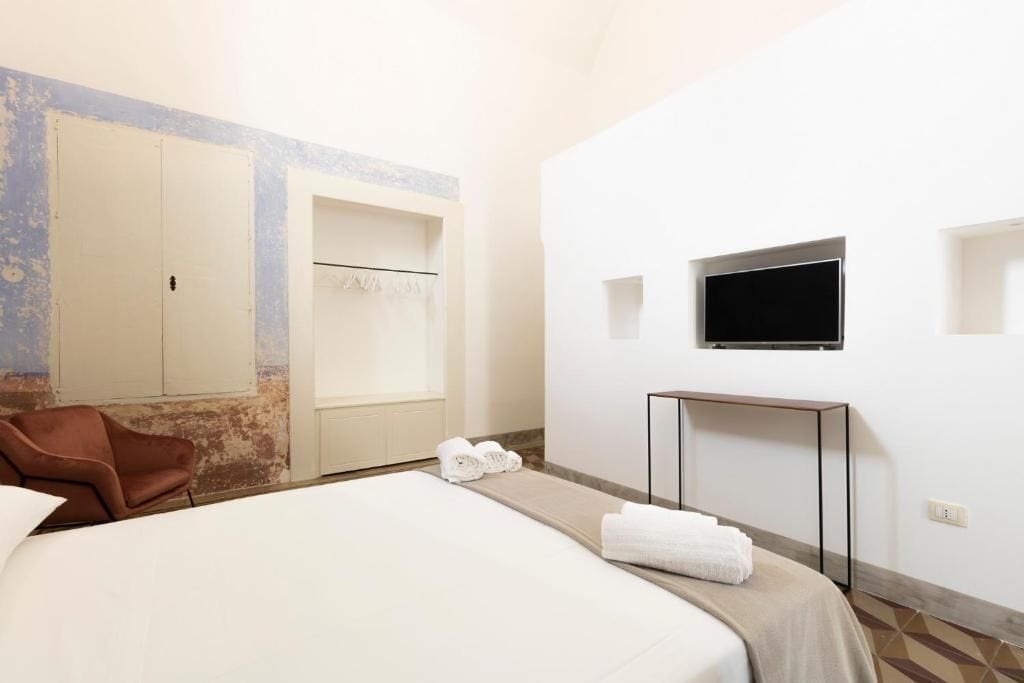 A hotel room with a bed, a TV mounted on the wall, a small table, and a chair.