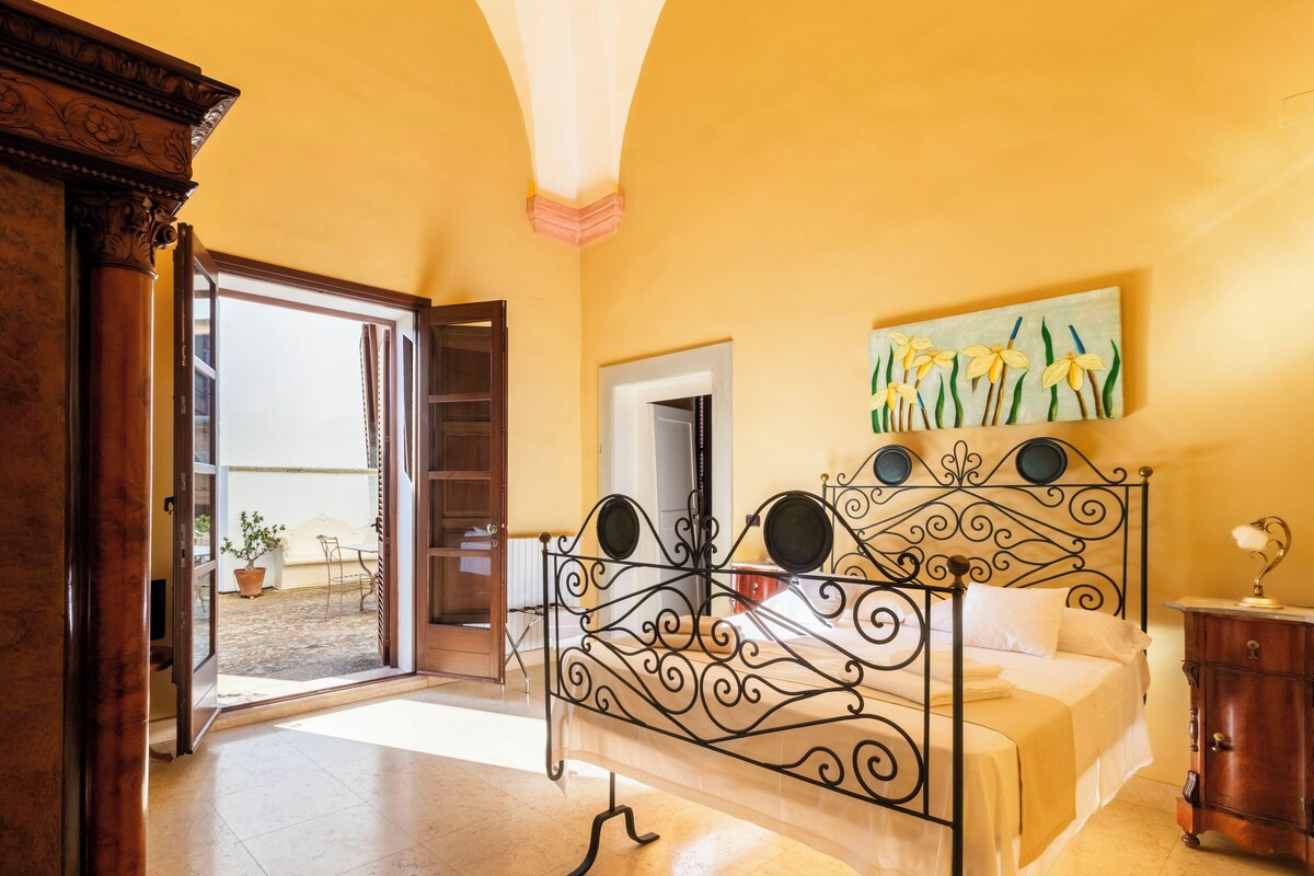 A bedroom with a bed, a nightstand, a painting, and a door leading to a balcony.