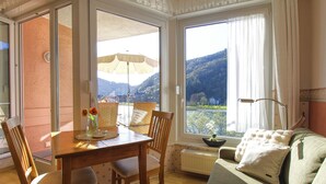A room with a wooden table, chairs, a sofa, a view of mountains through a window, and a radiator.