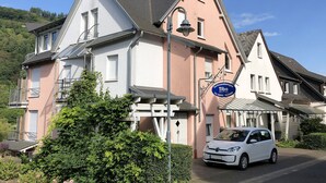 A two-story house with a balcony, a car parked in front, and a sign indicating it's a rental property.