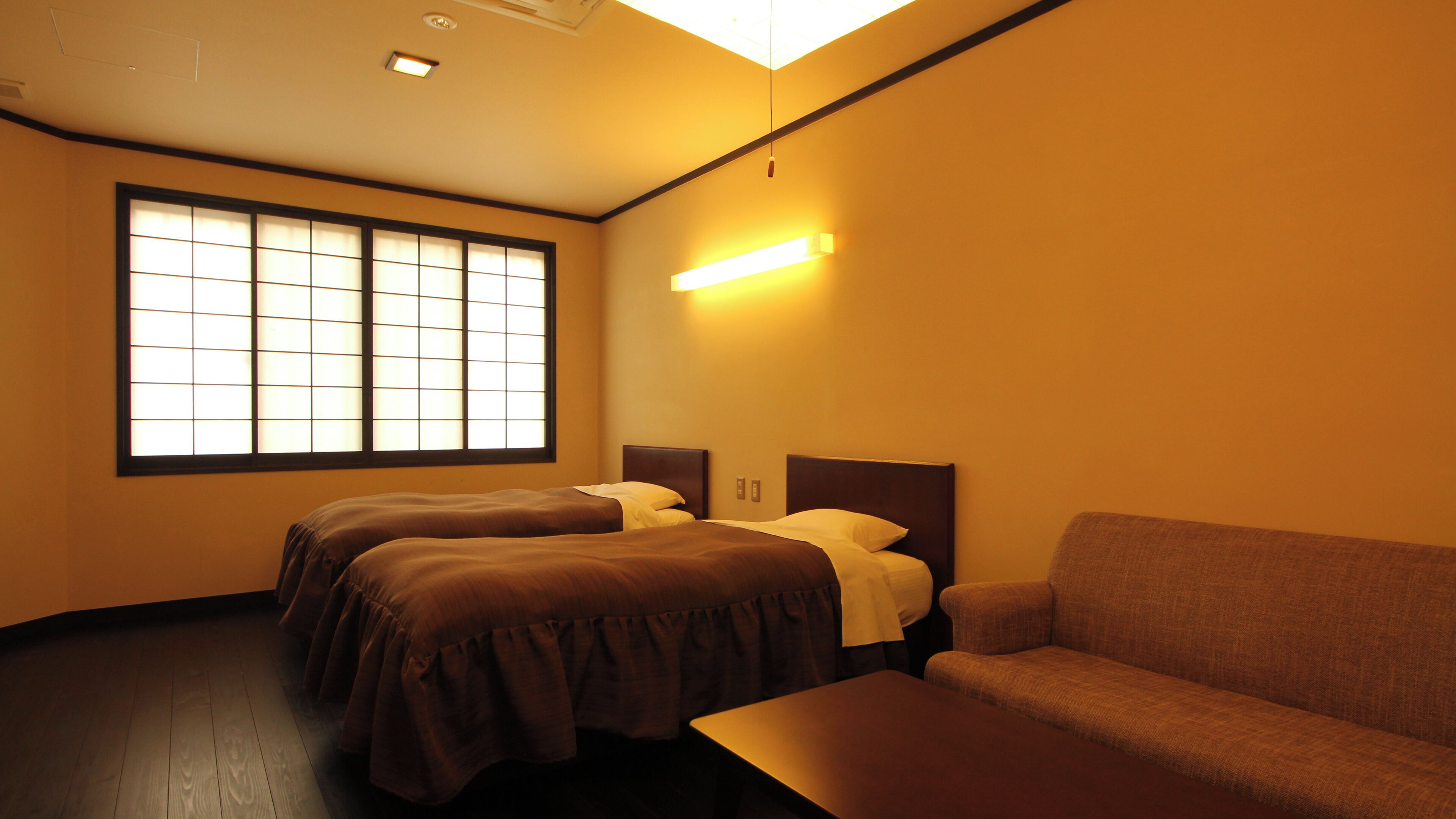 A hotel room with two beds, a sofa, a table, and a large window.