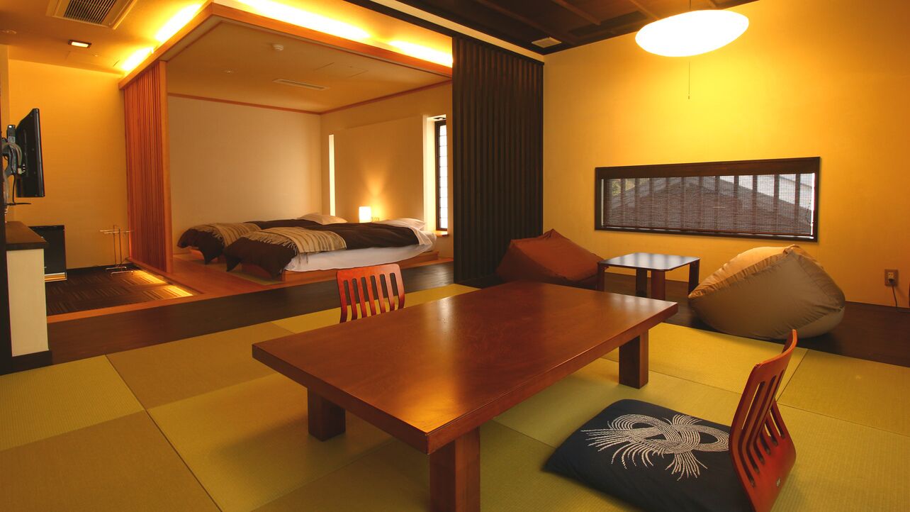 A hotel room with a wooden dining table, a sofa, a bed, and a large window.