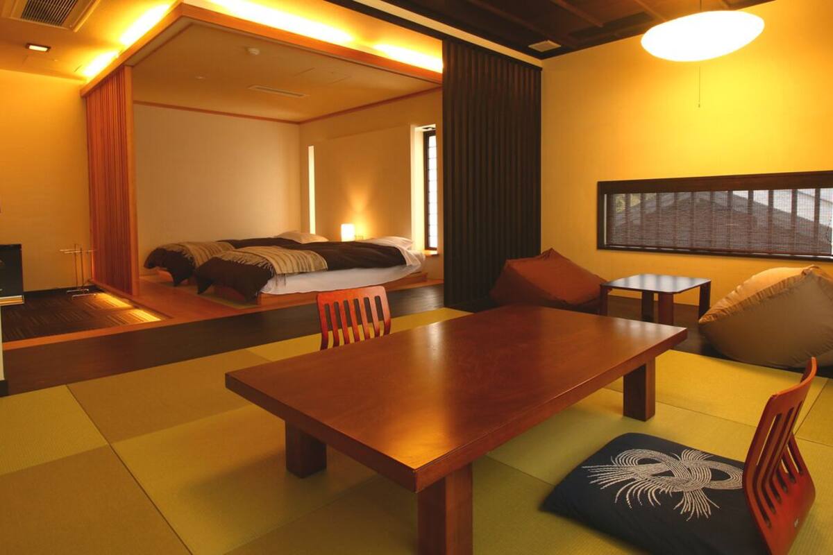 A hotel room with a wooden dining table, a sofa, a bed, and a large window.