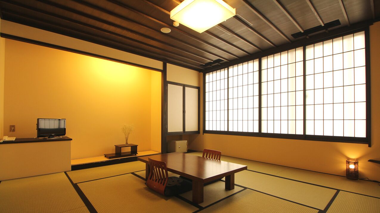 A traditional Japanese room with tatami flooring, a low table, chairs, a television, and sliding doors.