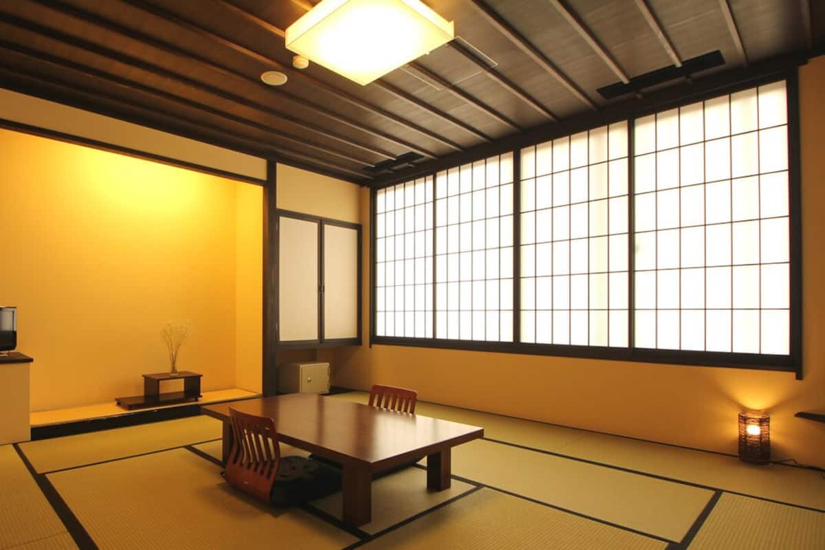 A traditional Japanese room with tatami flooring, a low table, chairs, a television, and sliding doors.