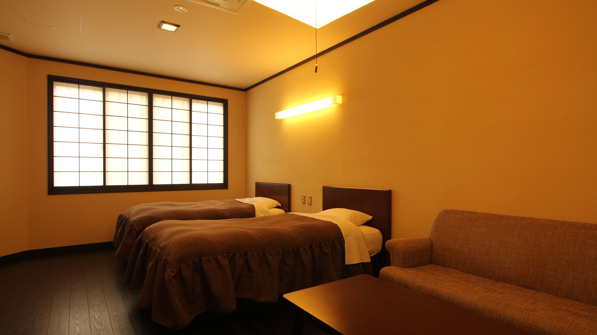 A hotel room with two beds, a sofa, and a large window.