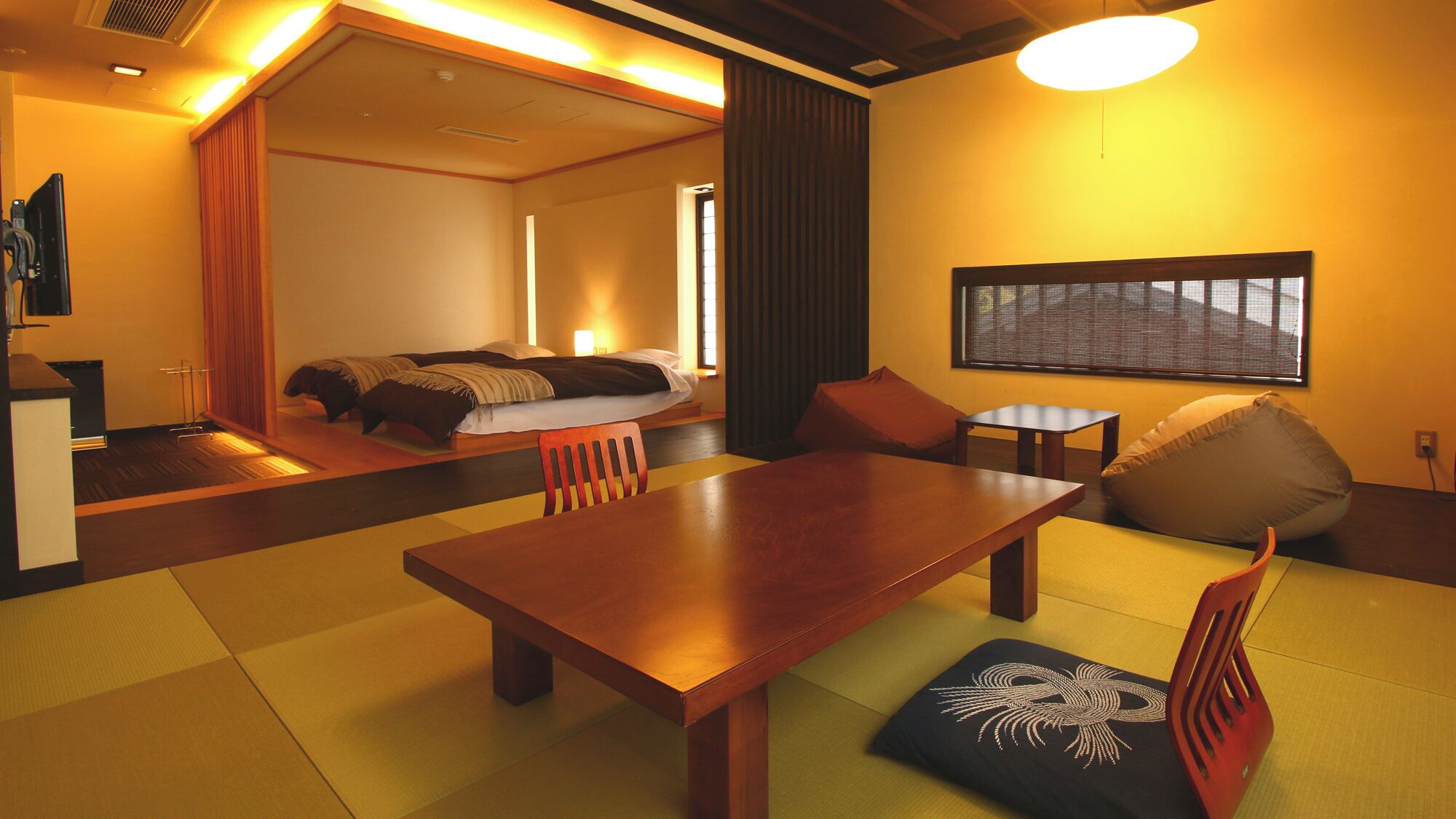 A hotel room with a wooden dining table, a sofa, a small table, and a window with blinds.