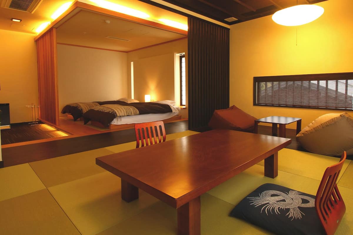 A hotel room with a wooden dining table, a sofa, a small table, and a window with blinds.