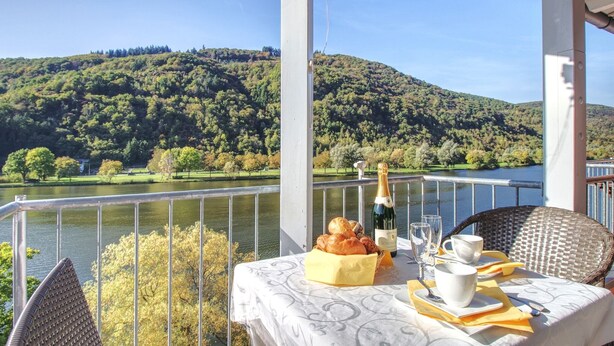 A balcony with a table set for breakfast, overlooking a lake and forested hills. - Apartment with balcony directly on the banks and with a view of the Moselle (Bullay)