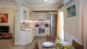 Eine moderne Küche mit weißen Schränken, einer Mikrowelle, einem Backofen und einem Kühlschrank. Es gibt einen Esstisch mit Stühlen und ein Gemälde an der Wand.
