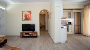 Ein modernes Wohnzimmer mit Flachbildfernseher, einer Holzunterhaltungseinheit und einem Essbereich, mit einer Küche im Hintergrund.