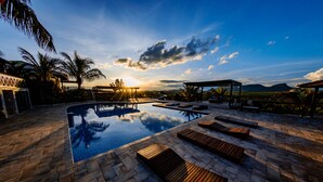 Zona de piscina con tumbonas de madera y una vista despejada del atardecer sobre un paisaje montañoso.